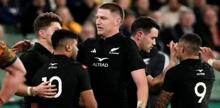 Joueurs des All Blacks en discussion sur le terrain, illustrant la cohésion d'équipe.