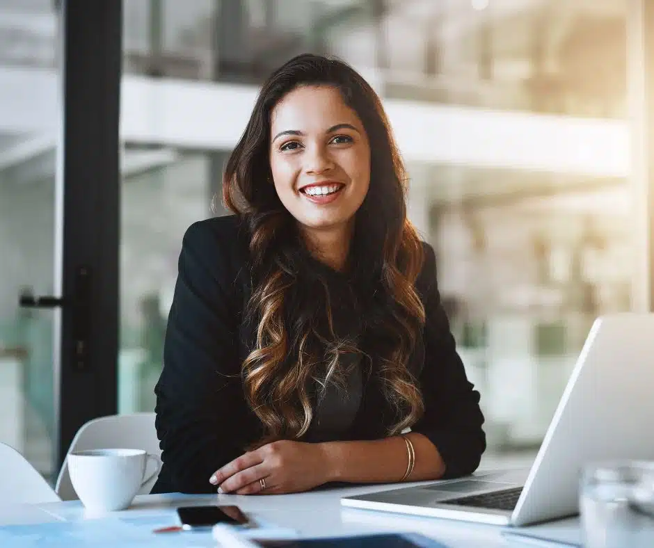 Femme professionnelle souriante assise devant son ordinateur dans un bureau moderne.