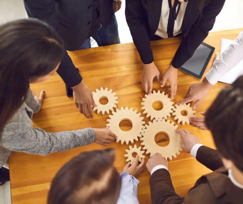 Équipe coordonnée ajustant des engrenages sur une table, métaphore de la collaboration.