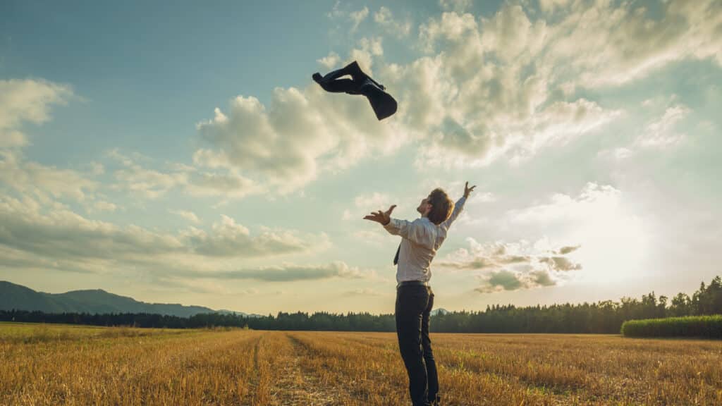 Entrepreneur joyeux lançant sa veste en l'air dans un champ au coucher du soleil, symbolisant la liberté en entrepreneuriat.