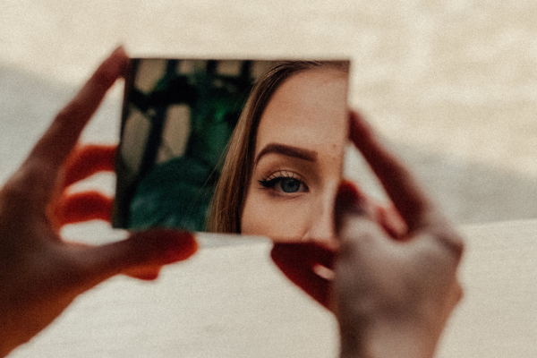 Femme tenant un miroir et observant son propre regard, symbole de la prise de conscience de soi et du travail sur l’ego au travail.