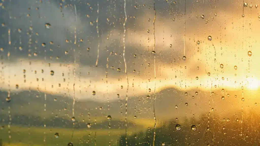 Gouttes de pluie sur une vitre avec un coucher de soleil en arrière-plan, symbole pour changer de regard au travail