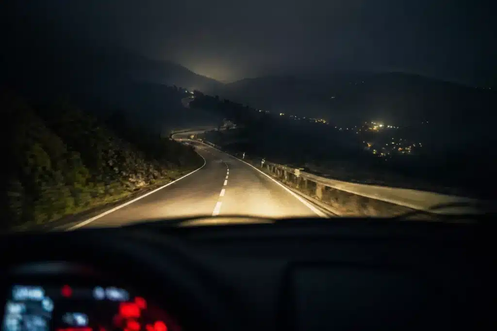 Route sinueuse de montagne éclairée par les phares la nuit, symbole d'avancer sans voir toute la route face à la procrastination
