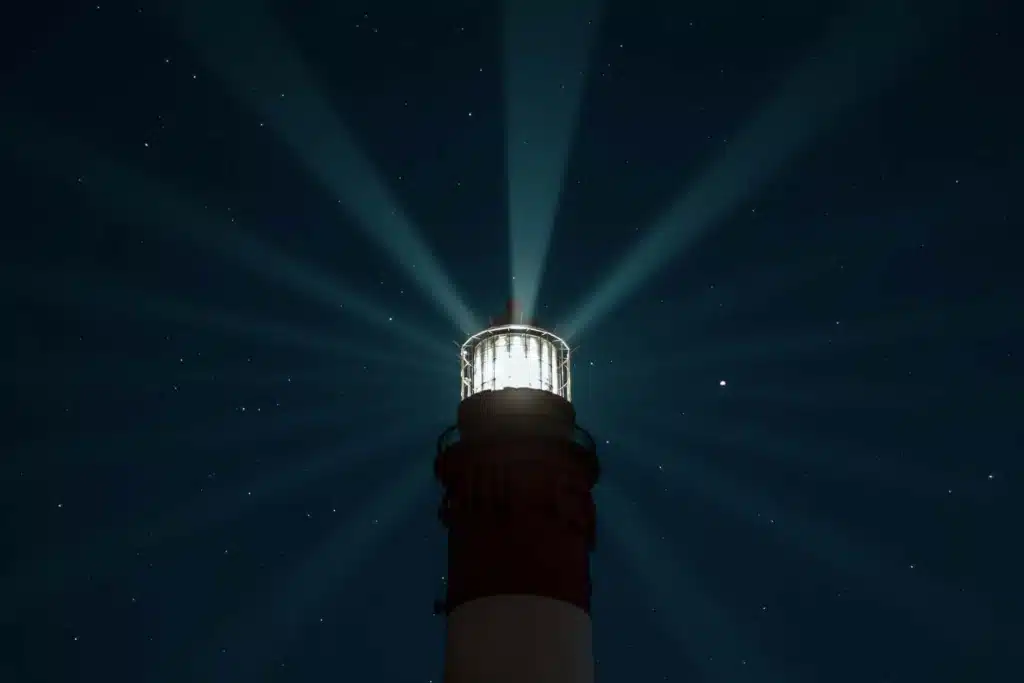 Phare diffusant sa lumière dans un ciel étoilé, symbole de la fréquence intérieure qui rayonne autour de soi