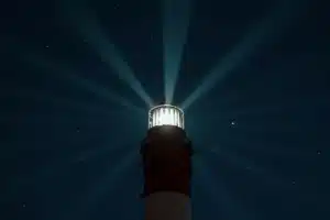 Phare diffusant sa lumière dans un ciel étoilé, symbole de la fréquence intérieure qui rayonne autour de soi